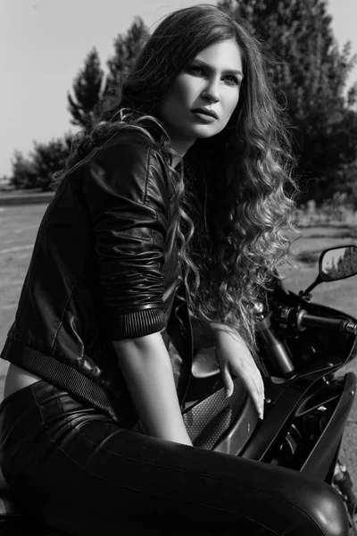 bir motosiklet yakınındaki deri giysili genç kadın. Siyah ve beyaz fotoğraf