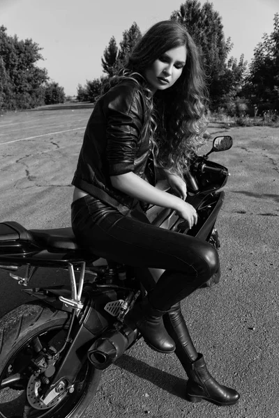 Jovem mulher em roupas de couro perto de uma motocicleta. Foto em preto e branco — Fotografia de Stock