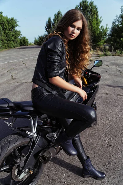 Jonge vrouw in de kleding van leder in de buurt van een motorfiets — Stockfoto