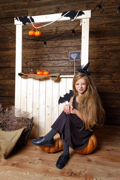 Niña vestida como una bruja se sienta en una calabaza. El concepto de Halloween — Foto de Stock