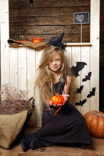Niña vestida como una bruja se sienta en una calabaza. El concepto de Halloween — Foto de Stock