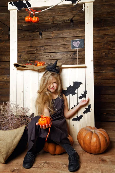 Niña vestida como una bruja se sienta en una calabaza. El concepto de Halloween — Foto de Stock