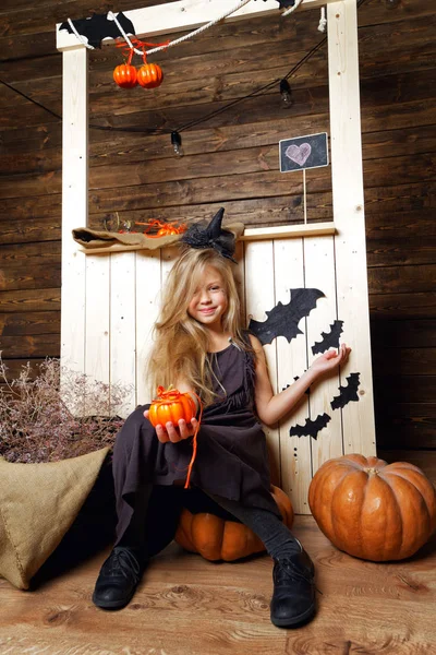 Niña vestida como una bruja se sienta en una calabaza. El concepto de Halloween — Foto de Stock