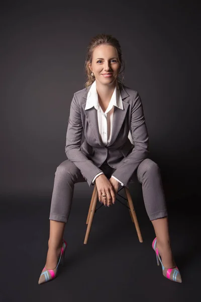 Senhora de negócios em terno senta-se em uma cadeira no fundo preto — Fotografia de Stock