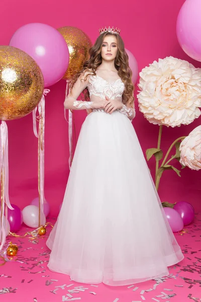 Jong meisje in jurk en kroon op roze achtergrond — Stockfoto