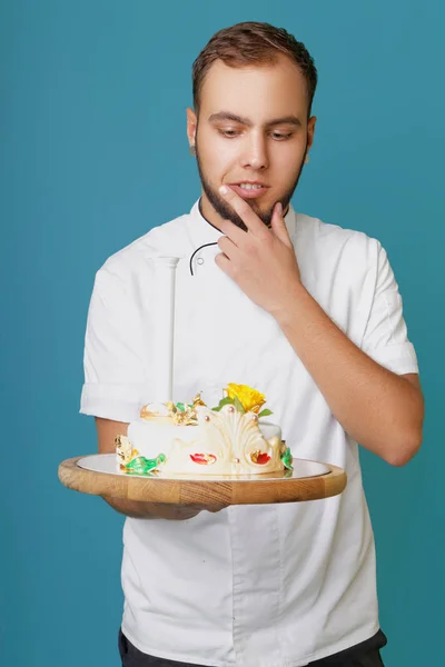 young male confectioner in a tunic with cake in the studio