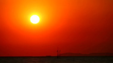 Günbatımı kızıl gökyüzü, arka tarafta karanlık bir yer ve geçen bir balıkçı teknesi.
