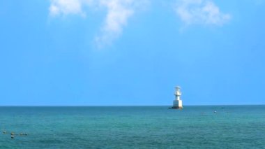 Beyaz bulut ve deniz feneri deniz ve mavi gökyüzünde mercan resifleriyle çevrilidir.