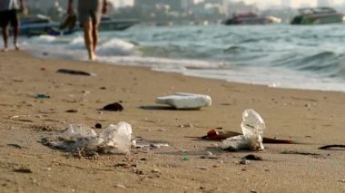 Plajda plastik kauçuk ve atıklarla yürüyen insanlar sahilde kalır ve dalgalar onları denize savurur.