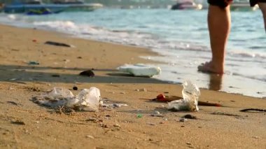 Plajda plastik lastik ve atıklarla yürüyen insanlar plajda kalır ve dalgalar onları denize savurur.