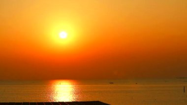 Denizde gün batımı ve yüzeyde güneş ışığı yansıması ve hareket eden küçük dalgalar.