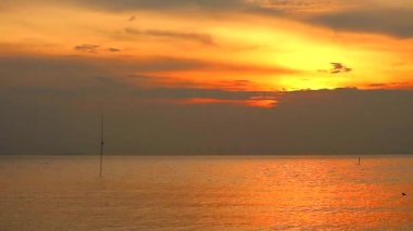 Günbatımı turuncu gökyüzü ve denizin üzerinde hareket eden koyu sarı bulut
