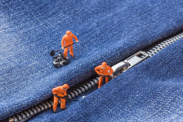 The concept for the fashion industry. Miniature workers repair the zipper on jeans, close up.