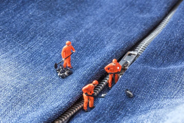 The concept for the fashion industry. Miniature workers repair the zipper on jeans, close up.