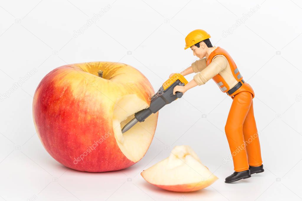 Miniature toy worker cutting an apple. Close-up view.