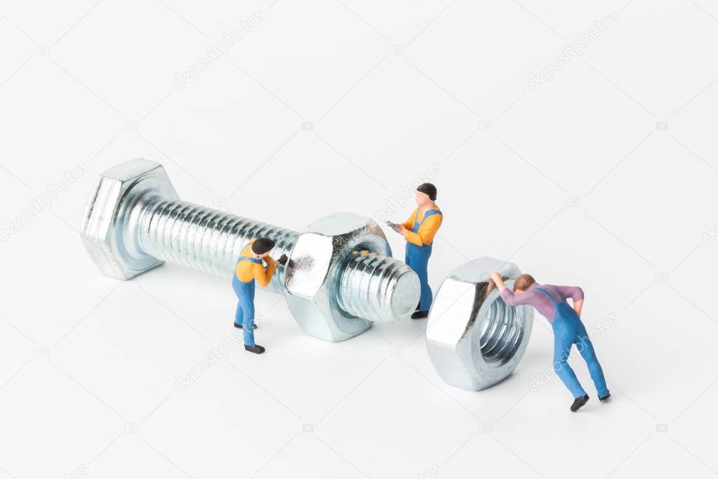 The concept of a collective solution to any problem. Miniature toy workers tightening a nut of a new bolt on white background. Close-up view.