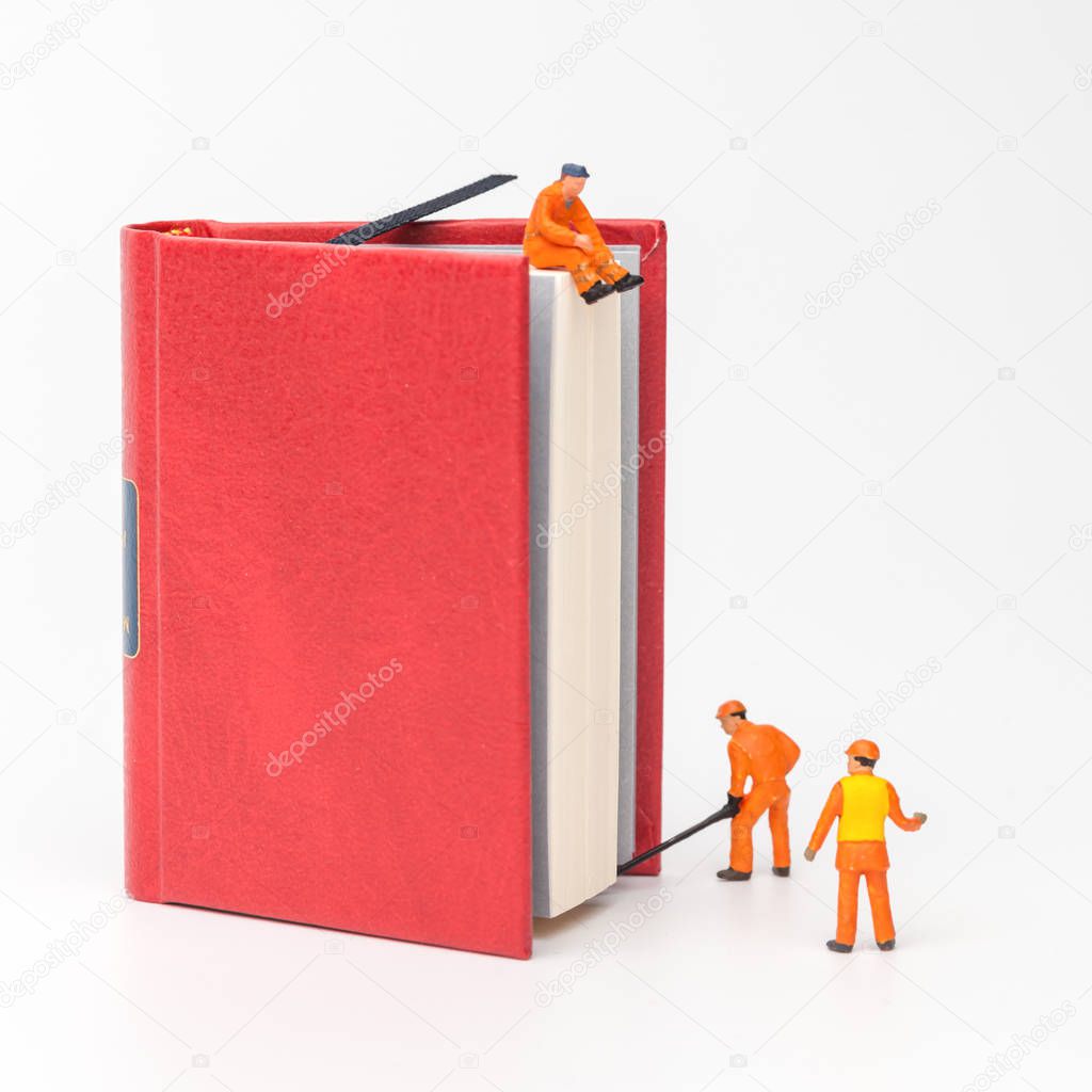 Miniature people. The concept of a collective solution to any problem. Miniature toy workers pulling a big book. Workers perform disposal of the Chief. Close-up view.