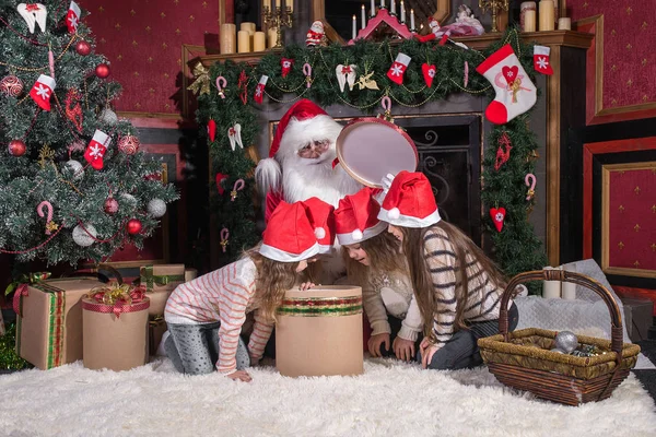 Santa Claus a děti otevření prezentuje na krb. — Stock fotografie