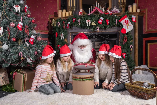 Santa Claus a děti otevření prezentuje na krb. — Stock fotografie