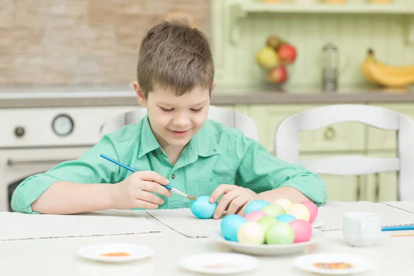 Маленький блондин мальчик раскрашивает яйца для пасхального отдыха на домашней кухне — стоковое фото
