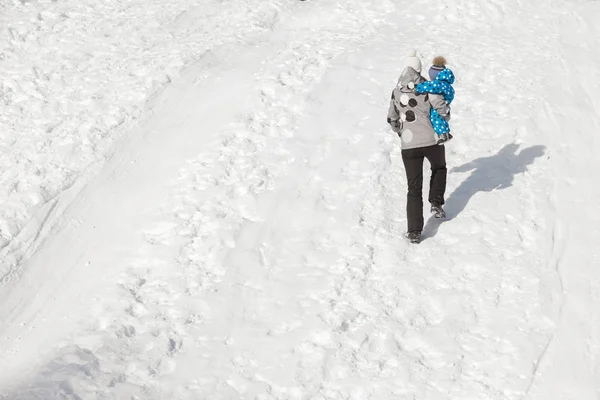 Mãe com filho sobe em uma colina nevada para cima — Fotografia de Stock