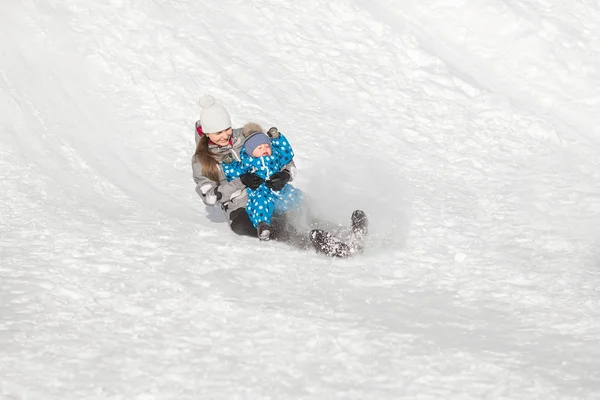 Mutter und Sohn rutschen an einem sonnigen Wintertag einen Schneehügel hinunter — Stockfoto