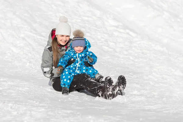 Retrato de la madre con el hijo en un día de invierno, la familia se sienta en la nieve y riendo — Foto de Stock
