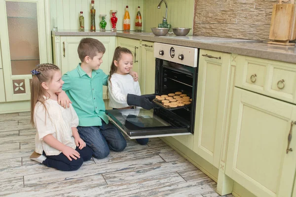 Troje dzieci patrząc na pliki cookie w piecu w kuchni — Zdjęcie stockowe