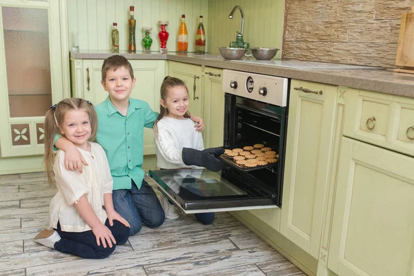 stock image Three children looking at the cookies in the oven in the kitchen