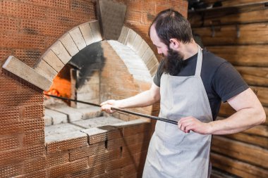 Yemek pişirmek için fırın pişirme ve kömürlerin poker ile karıştırılır erkek Baker