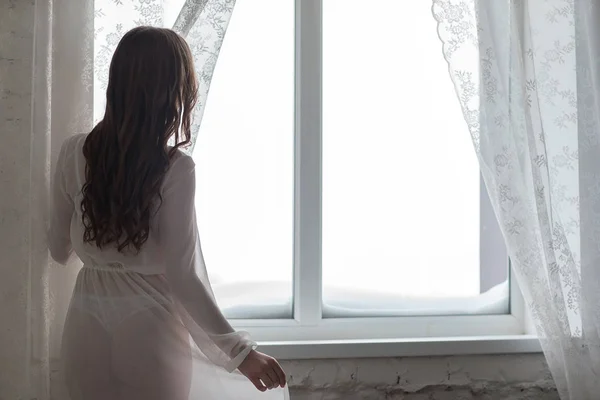 Femme frappante se tient devant la fenêtre et regarde à l'extérieur . — Photo