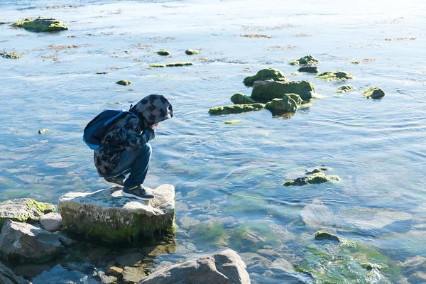 Un niño se para en una roca en el mar negro y mira hacia el agua — Foto de Stock