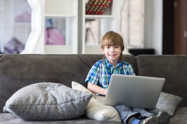 Evdeki kanepede dizüstü bilgisayar kullanan küçük çocuk.