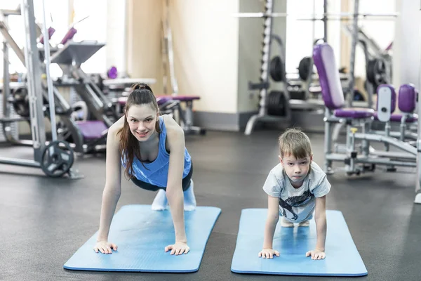 mother and son in sport shirts are doing plank in gym