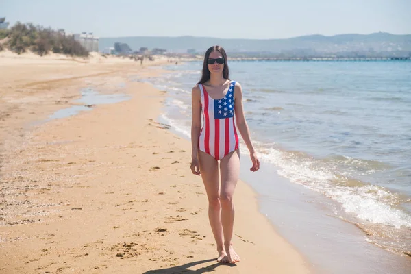 Стройная молодая женщина под флагом США идет вдоль побережья — стоковое фото