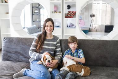 Anne ile oğlu kanepe ve tutmak İngilizce bulldog köpek yavrusu üzerinde oturan