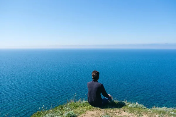 Homme assis sur le bord de la falaise au bord — Photo