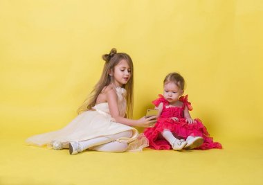 Elbiseler sarı bir arka plan üzerinde iki kız kardeş kendilerini telefonla fotoğrafı