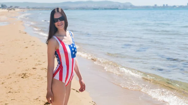 Una joven esbelta en una bandera de los Estados Unidos camina por la costa — Foto de Stock