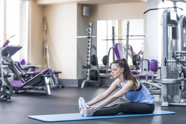 Portret van gelukkige jonge vrouw doen stretching oefening in gym — Stockfoto
