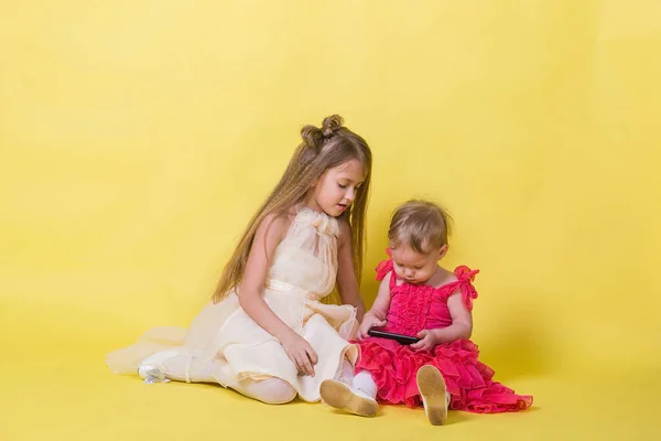 Zwei Schwestern in Kleidern auf gelbem Hintergrund und einem mobilen Smartphone — Stockfoto