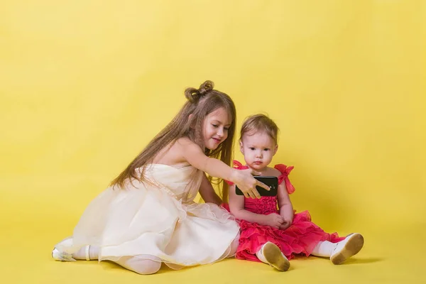 Zwei Schwestern in Kleidern vor gelbem Hintergrund fotografierten sich am Telefon — Stockfoto