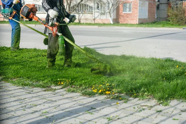 男は身に着けているオーバー オールとゴムブーツ緑の草を刈っていてガソリンの芝生のトリマー. — ストック写真