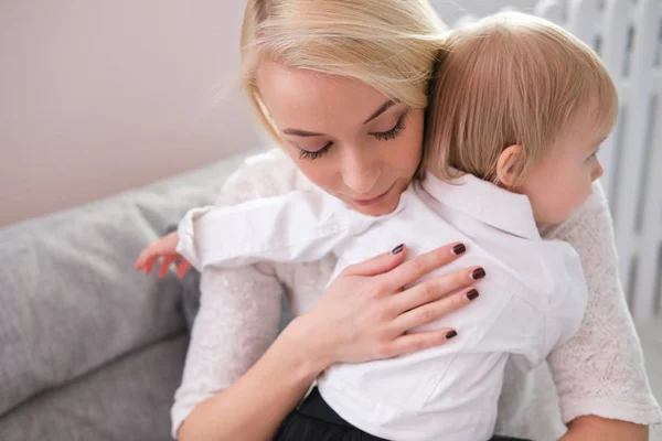Ung mamma hålla en baby dotter i hennes armar och kysser henne i barnkammaren — Stockfoto