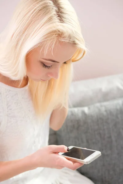 Retrato de la joven feliz con el teléfono móvil sentado en el sofá en casa — Foto de Stock