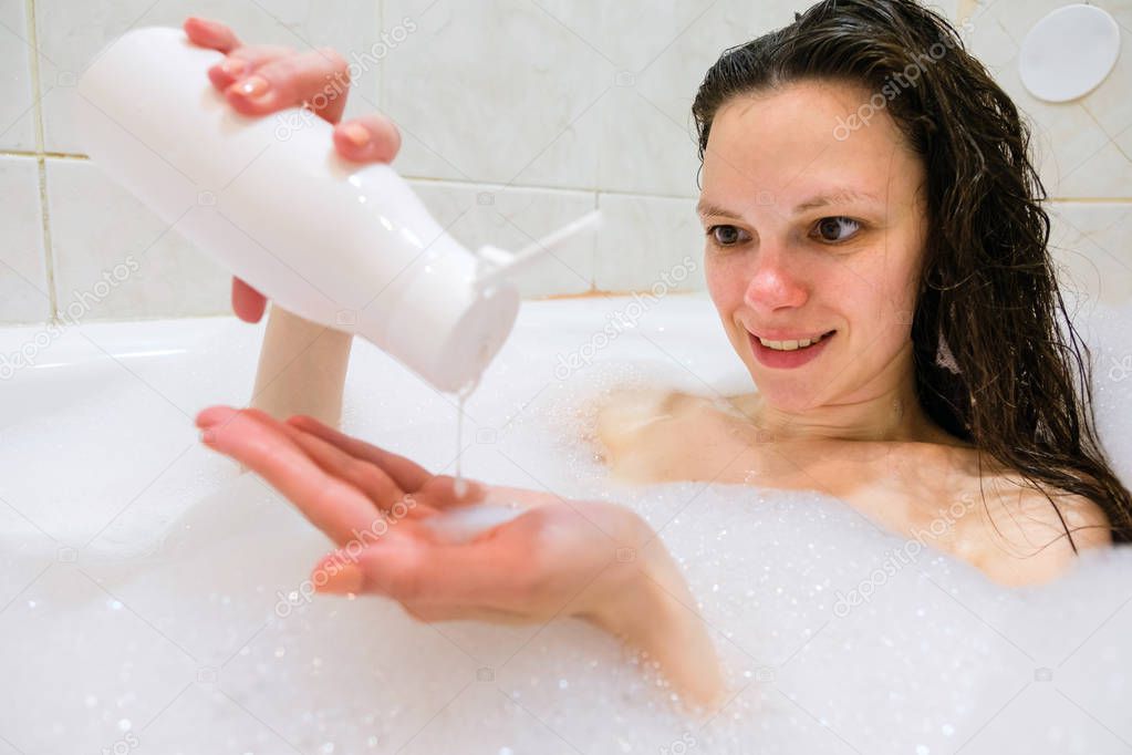 Brunette woman pouring shampoo on hand in shower