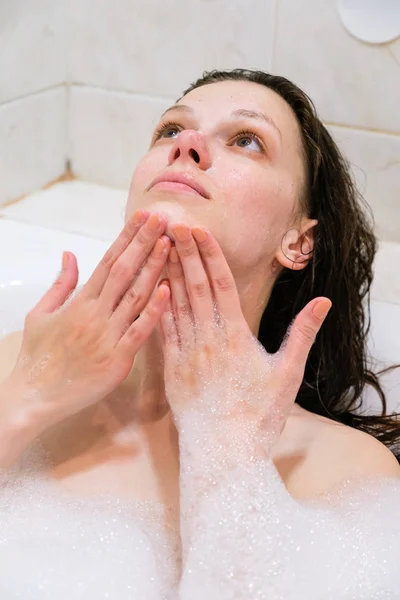 Gyönyörű nő arcát a hab kezelés a fehér fürdőszoba tisztító — Stock Fotó