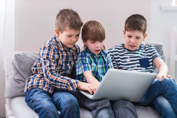 Los niños en casa sentados en el sofá, jugando con el ordenador portátil — Foto de Stock