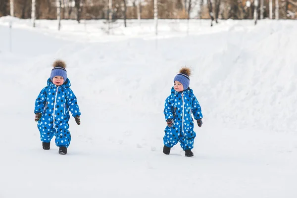 Мальчики-близнецы, гуляющие по парку зимой в одинаковых комбинезонах — стоковое фото