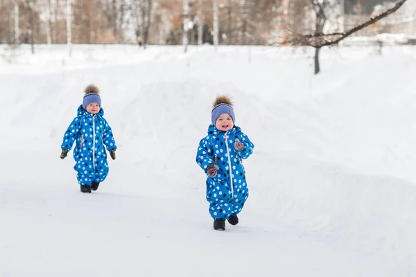 Мальчики-близнецы, гуляющие по парку зимой в одинаковых комбинезонах — стоковое фото